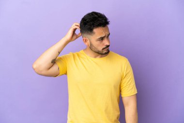 Kafkasyalı genç bir adam mor arka planda izole edilmiş, kafası kaşınırken şüpheleri var.