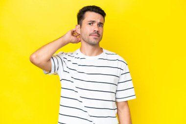 Soyutlanmış sarı arka planı olan yakışıklı bir genç. Şüpheleri var.