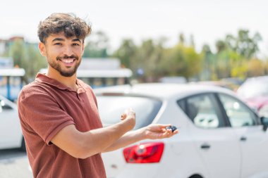 Genç Arap yakışıklı adam dışarıda arabanın anahtarlarını tutarken neşeli bir ifadeyle.