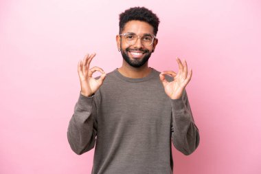 Pembe arka planda izole edilmiş genç Brezilyalı iki eliyle tamam işareti gösteriyor.
