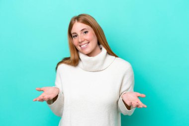 Genç kızıl saçlı kadın mavi arka planda yalnız mutlu ve gülümsüyor.