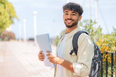 Açık havada gülümseyen genç bir Arap öğrenci.