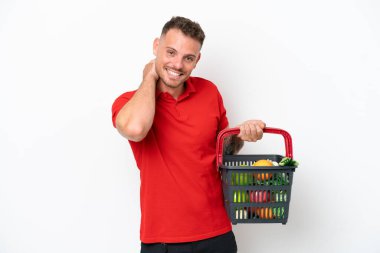 Beyaz arka planda izole edilmiş yiyecek dolu bir alışveriş sepeti tutan beyaz bir adam.