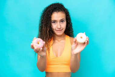 Genç bir Arap kadın mavi arka planda izole edilmiş elinde donut ve üzgün