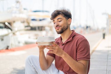 Genç Arap yakışıklı adam açık havada bir paket yemek alıyor.