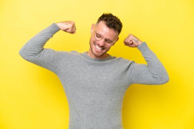 Sarı arka planda izole edilmiş beyaz, yakışıklı genç adam güçlü bir jest yapıyor.