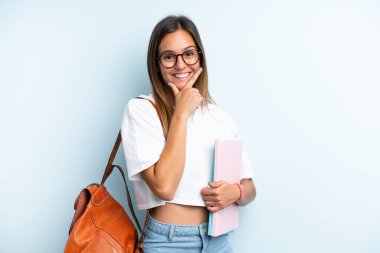 Mavi arka planda izole edilmiş genç bayan mutlu ve gülümsüyor.