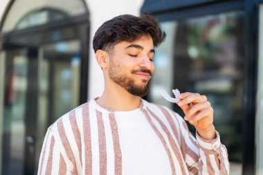 Dışarıdaki yakışıklı Arap adam görünmez diş telleri tutuyor.