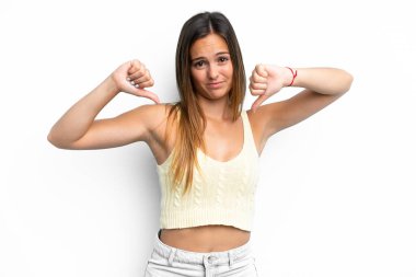 Beyaz arka planda izole edilmiş genç beyaz kadın baş parmağını iki eliyle aşağı gösteriyor.