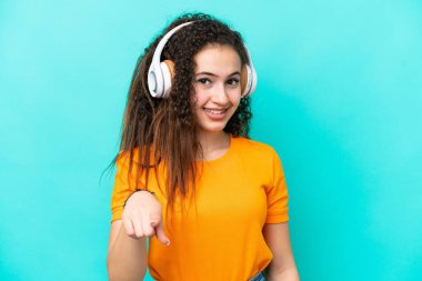 Genç Arap kadın mavi arka planda izole edilmiş müzik dinliyor.