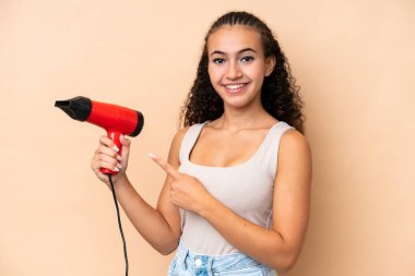 Elinde bej arka planda izole edilmiş bir saç kurutma makinesi tutan genç bir kadın.