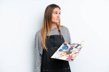 Beyaz arka planda izole edilmiş bir palet tutan beyaz kadın yan tarafa bakıyor.