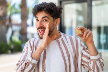 Yakışıklı bir Arap elinde Bitcoin ile dışarıda bir şeyler fısıldıyor.