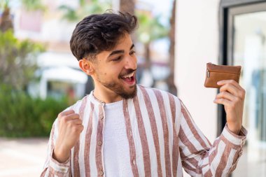 Yakışıklı bir Arap, dışarıda cüzdan tutuyor ve zaferi kutluyor.