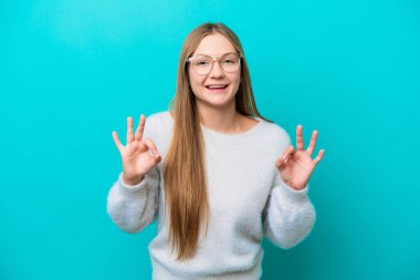 Mavi arka planda izole edilmiş genç bir Rus kadın iki eliyle tamam işareti gösteriyor.