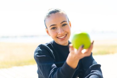 Genç Faslı kız açık havada elinde mutlu bir ifadeyle bir elma tutuyor.