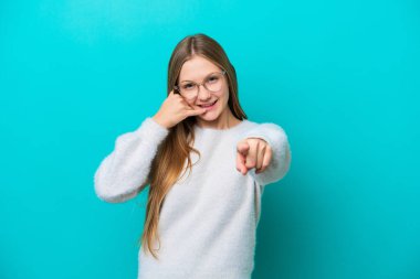 Mavi arka planda izole edilmiş genç bir Rus kadın telefon hareketi yapıyor ve ön tarafı işaret ediyor.