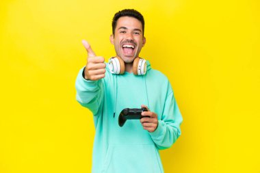 Genç yakışıklı bir adam, izole bir duvarın üzerinde bilgisayar oyunu kontrolörüyle oynuyor. Başparmakları havada, çünkü iyi bir şey oldu.