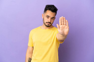 Mor arka planda izole edilmiş genç beyaz adam dur hareketi yapıyor.