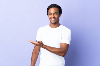 Örgülü genç Afrikalı Amerikalı adam mor arka planda izole edilmiş bir fikir sunuyor ve gülümsüyor.