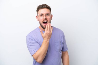 Beyaz arka planda izole edilmiş genç beyaz bir adam esniyor ve geniş bir ağzı eliyle kapatıyor.