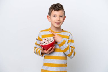 Beyaz arka planda yalıtılmış mısır gevreği kasesi tutan küçük beyaz çocuk bir ürün sunmak için yan tarafı işaret ediyor.