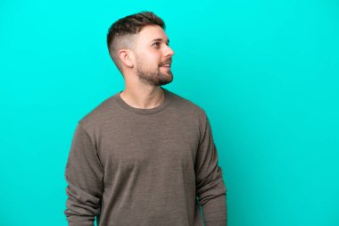 Kafkasyalı genç adam mavi arka planda izole edilmiş, yana bakıyor ve gülümsüyor.