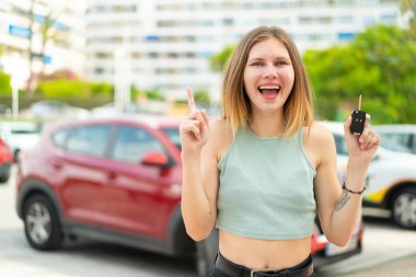 Dışarıda arabanın anahtarlarını tutan genç sarışın kadın harika bir fikri işaret ediyor.