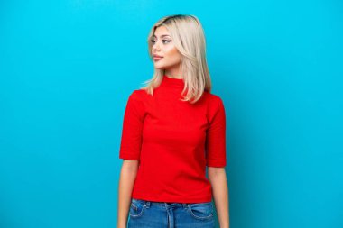 Mavi arka planda izole edilmiş genç Rus kadın yan tarafa bakıyor.