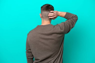 Kafkasyalı genç adam mavi arka planda izole edilmiş ve düşünüyor.