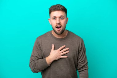 Mavi arka planda izole edilmiş genç beyaz adam sağa bakarken şaşırdı ve şok oldu.