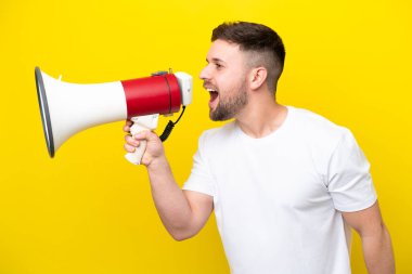 Sarı arka planda izole edilmiş genç beyaz bir adam megafondan bir şey duyurmak için bağırıyor.
