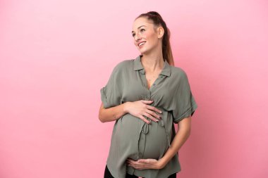 Pembe arka planda izole genç bir kadın hamile ve mutlu.