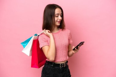 Genç Ukraynalı bir kadın pembe arka planda izole edilmiş. Elinde alışveriş çantaları var ve bir arkadaşına cep telefonuyla mesaj yazıyor.