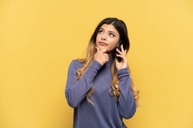Sarı arka planda izole edilmiş cep telefonu kullanan genç Rus kız.