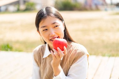Açık havada genç bir Çinli kadın elinde mutlu bir ifadeyle bir elma tutuyor.