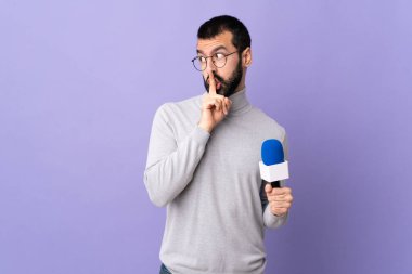 Mor arka planda mikrofon tutan sakallı yetişkin bir muhabir sessizlik işareti gösteriyor. Parmağını ağzına sokuyor.