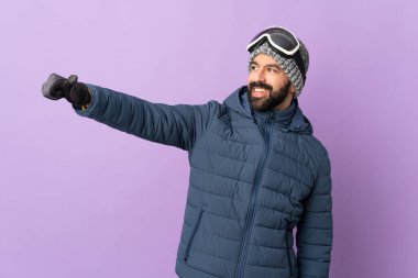 İzole edilmiş mor arka planda snowboard gözlüklü kayakçı iyi niyet gösterisi yapıyor.