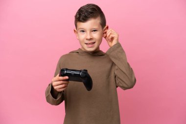 Pembe arka planda izole edilmiş bir bilgisayar oyunu kontrolörüyle oynayan küçük beyaz çocuk hayal kırıklığına uğramış ve kulaklarını tıkamış.