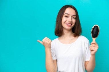 Mavi arka planda saç tarağı olan genç Ukraynalı kadın bir ürünü sunmak için kenarı işaret ediyor.