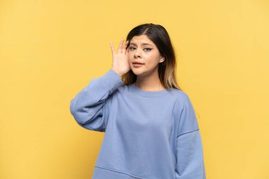 Sarı arka planda izole edilmiş genç bir Rus kız. Kulağına elini sürerek bir şeyler dinliyor.