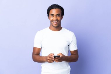 Örgülü genç Afrikalı Amerikalı adam mor arka planda izole edilmiş şaşırmış ve bir mesaj gönderiyor.