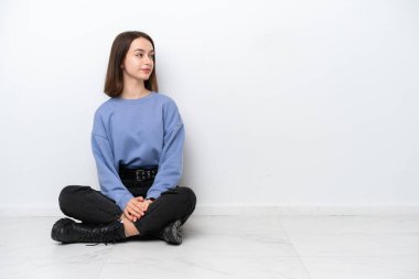 Yerde oturan genç Ukraynalı kadın beyaz arka planda yan pozisyonda izole edilmiş.