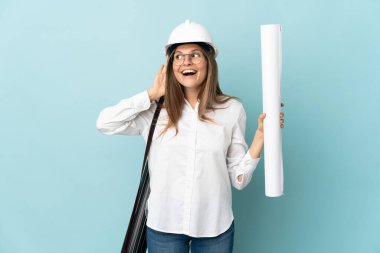 Slovak mimar kız elinde mavi arka planda izole edilmiş planlar tutuyor. Kulağına elini sürerek bir şeyler dinliyor.