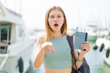 Açık havada pasaportu olan genç sarışın kadın şaşırmış ve ön tarafı işaret ediyor.