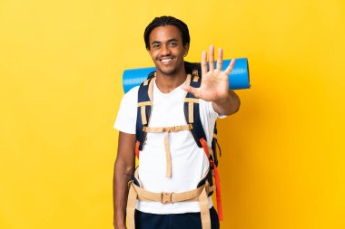 Sarı arka planda büyük bir sırt çantalı genç dağcı beş parmaklı sayıyor.