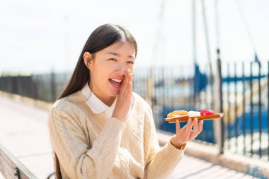 Genç Çinli kadın elinde sashimi ile dışarıda bir şeyler fısıldıyor.