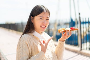 Genç Çinli bir kadın açık havada sashimi tutuyor ve onu doğrultuyor.