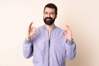 Sakallı, ceketli, soyutlanmış arka planda beyaz bir adam iki eliyle tamam işareti gösteriyor.