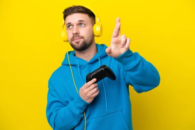 Sarı arka planda izole edilmiş bir bilgisayar oyunu kontrolörüyle oynayan beyaz bir adam.